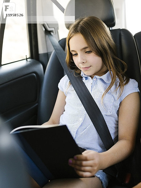Mädchen ( 8-9) sitzt im Auto und liest ein Buch