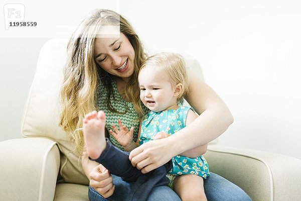 Mutter  die ihre Tochter (11-17 Monate) im Wohnzimmer anzieht