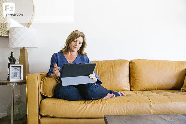 Frau benutzt digitales Tablet auf Sofa