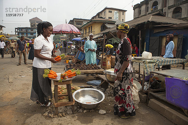 Eine Frau kauft Karotten auf dem Markt in Nigeria  Westafrika  Afrika