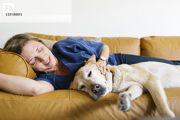 Frau und Labrador Retriever liegen auf dem Sofa