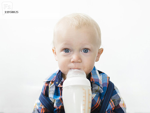 Studioaufnahme eines Jungen (12-17 Monate)  der aus einer Babyflasche trinkt