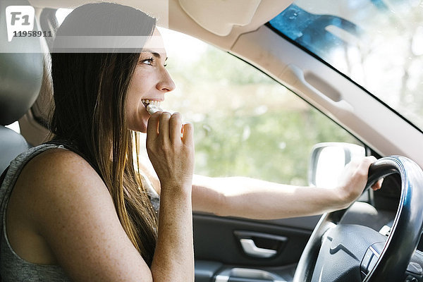 Lächelnde Frau fährt Auto und isst Brezel