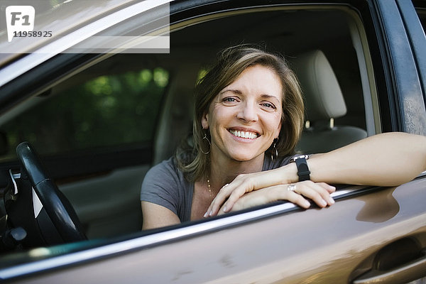 Porträt einer lächelnden Frau  die durch ein Autofenster schaut