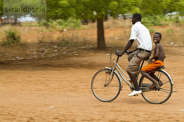 Ein Schuljunge wird auf dem Rücken eines Fahrrads nach Hause gebracht  Ghana  Westafrika  Afrika