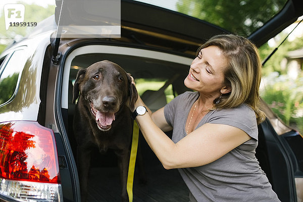 Frau mit Labrador Retriever an der Leine im Kofferraum eines Autos