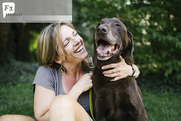 Lächelnde Frau im Gras sitzend mit Labrador Retriever