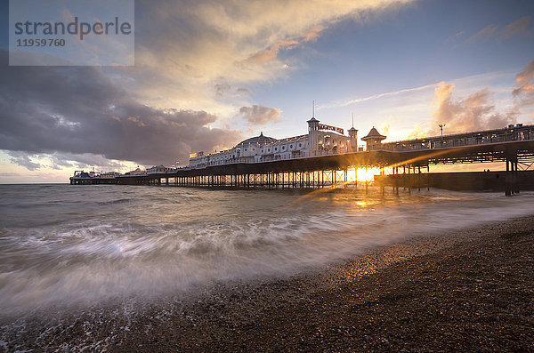 Brighton Pier bei Sonnenuntergang mit dramatischem Himmel und Wellen  die an den Strand gespült werden  Brighton  East Sussex  England  Vereinigtes Königreich  Europa