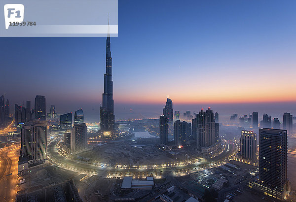 Stadtbild von Dubai  Vereinigte Arabische Emirate in der Abenddämmerung  mit dem Wolkenkratzer Burj Khalifa und beleuchteten Gebäuden im Vordergrund.