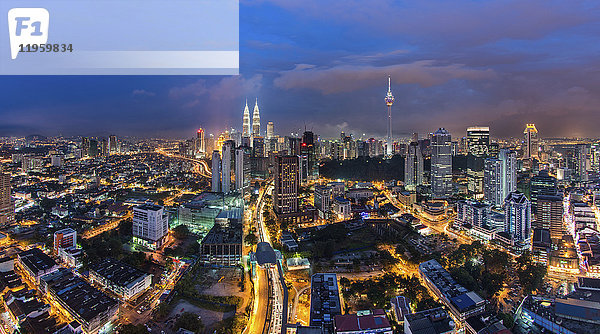 Stadtlandschaft von Kuala Lumpur  Malaysia in der Abenddämmerung  mit beleuchteten Petronas-Türmen und Kommunikationsturm in der Ferne.