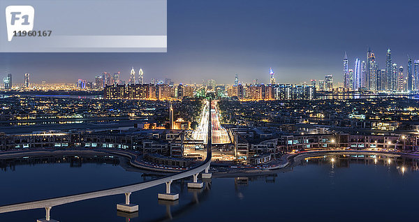 Stadtbild von Dubai  Vereinigte Arabische Emirate in der Dämmerung  mit beleuchteten Wolkenkratzern in der Ferne und einer Brücke über den Yachthafen im Vordergrund.