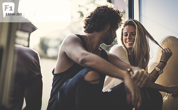 Ein Mann mit braunen Haaren in zerrissenen Jeans und eine Frau mit langen blonden Haaren sitzen im Freien  schauen sich an und lächeln.