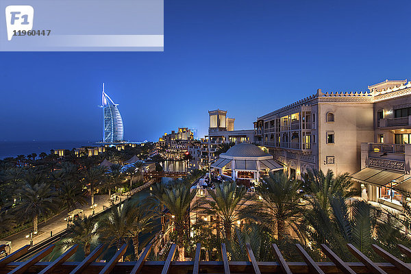 Stadtbild von Dubai  Vereinigte Arabische Emirate in der Abenddämmerung  mit beleuchteten Gebäuden und dem Burj Al Arab in der Ferne.