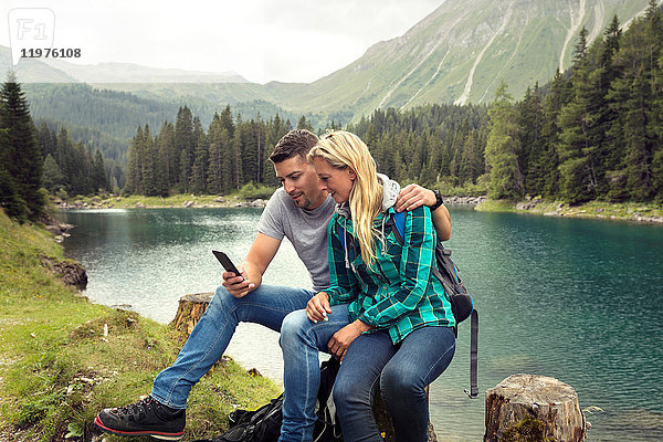 Paar wandert  sitzt am See und schaut auf das Smartphone  Tirol  Steiermark  Österreich  Europa
