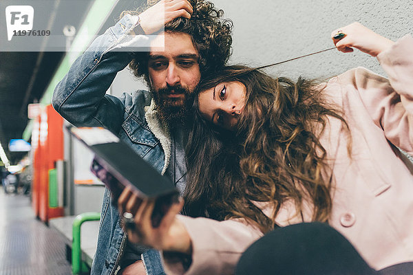 Junges Paar sitzt im Bahnhof  schaut auf Smartphone  besorgte Gesichtsausdrücke