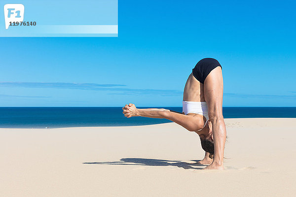 Seitenansicht einer Frau am Strand  die sich in Yogastellung nach vorne beugt