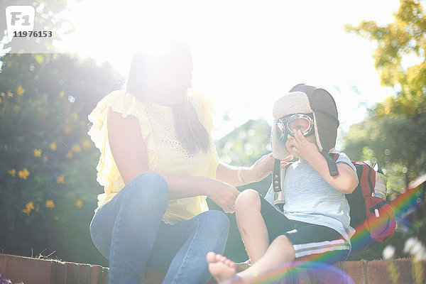 Junge mit Mutter im sonnenbeschienenen Garten setzt Piloten-Fliegerbrille auf