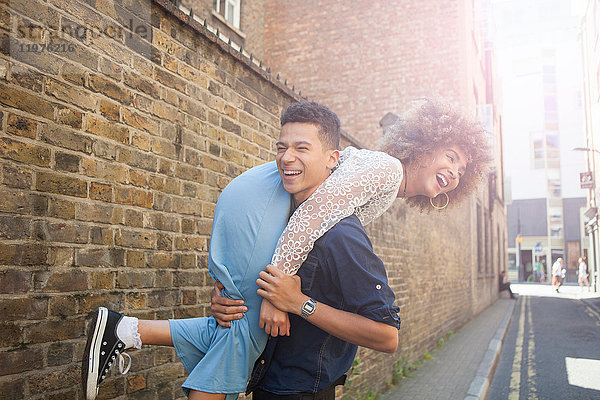 Junges Paar albert auf der Straße herum  Mann trägt Frau über die Schulter