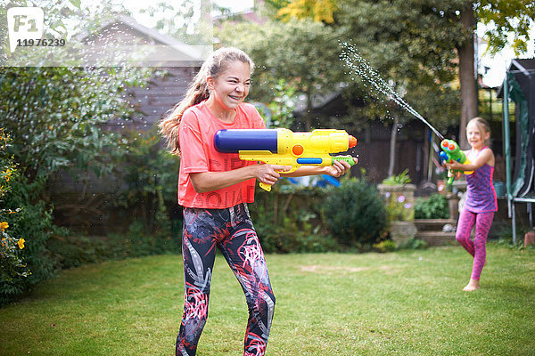 Teenager-Mädchen und ihre Schwester haben eine Wasserpistolenschlacht im Garten