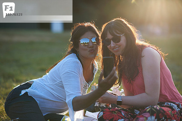 Zwei reife Freundinnen beim Smartphone-Selfie-Festival im Park  London  Großbritannien