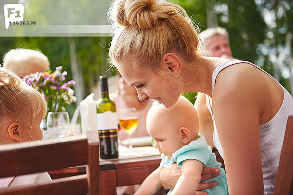 Junge Frau mit Baby- und Kleinkind-Töchtern beim Familienessen auf der Terrasse