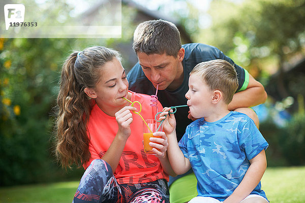 Reifer Mann mit Teenager-Tochter und Sohn teilen sich frischen Smoothie im Garten