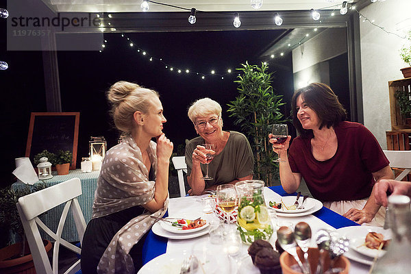 Drei Frauen sitzen am Esstisch und trinken aus Weingläsern