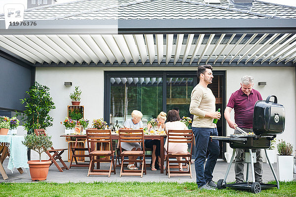 Zwei Männer grillen beim Familienessen auf der Terrasse