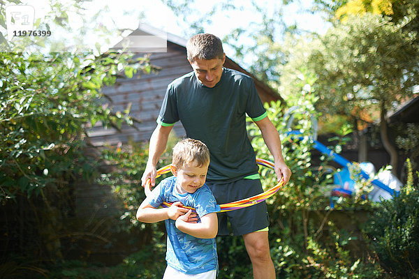 Junge und Vater spielen mit Kunststoffreifen im Garten