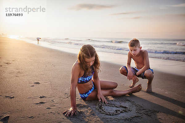 Mädchen malt Herz im Sand am Strand