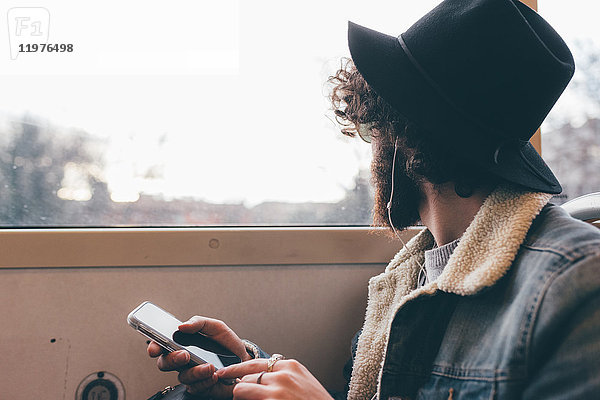 Junger Mann sitzt in der U-Bahn  hält ein Smartphone in der Hand und schaut aus dem Fenster