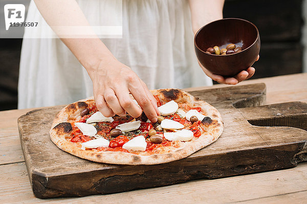 Frau legt Oliven auf hausgemachte Pizza  Mittelteil