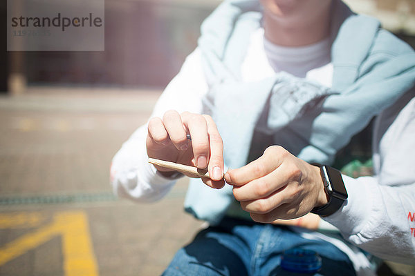 Junger Mann sitzt im Freien  dreht sich eine Zigarette  Mittelteil