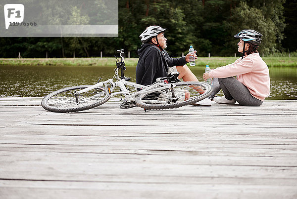 Ein erwachsenes Paar entspannt sich auf einem Steg am See  mit Fahrrädern hinter sich