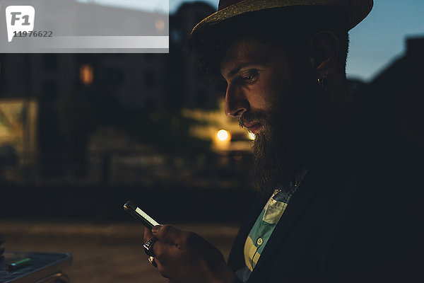 Mann auf der Straße schaut nachts auf Smartphone