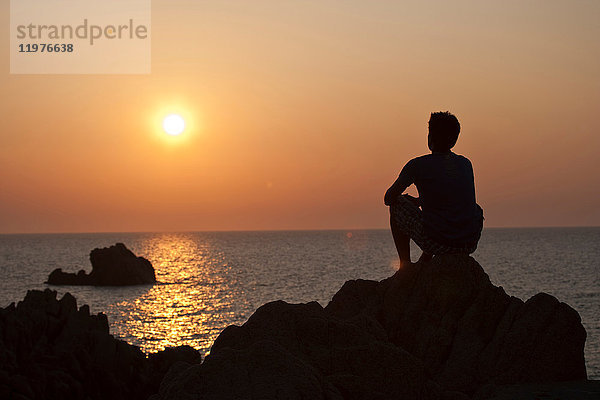 Silhouette eines Mannes auf Felsen  der den Sonnenuntergang über dem Meer betrachtet  Olbia  Sardinien  Italien