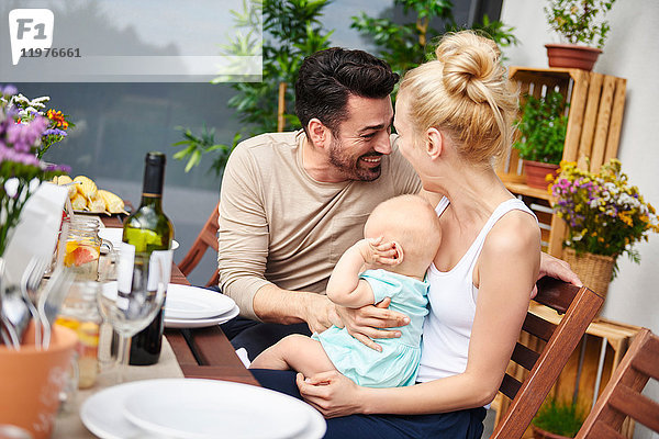 Glückliches Paar mit kleiner Tochter beim Familienessen auf dem Terrassentisch