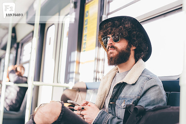 Junger Mann sitzt in der U-Bahn und benutzt ein Smartphone