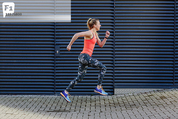 Junge weibliche Läuferin läuft mit hoher Geschwindigkeit über den Bürgersteig