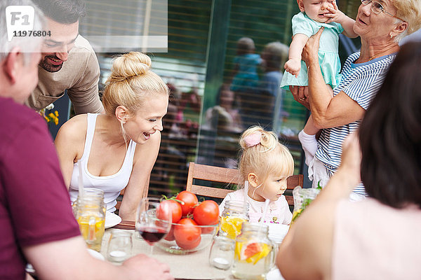 Drei-Generationen-Familie mit einem kleinen Mädchen und einem weiblichen Kleinkind beim Familienessen auf dem Terrassentisch