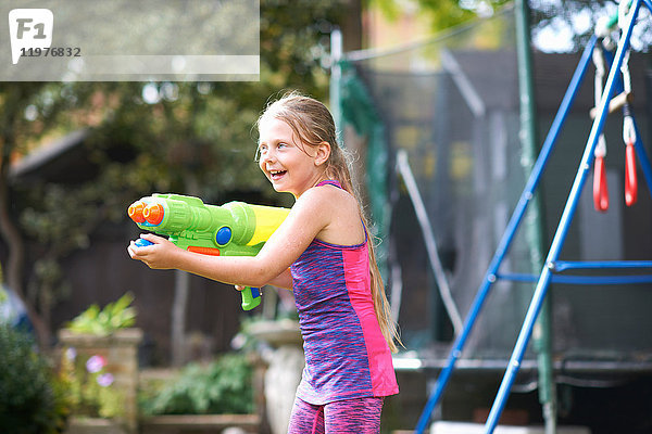 Mädchen mit nassem Haar hält Wasserpistole im Garten