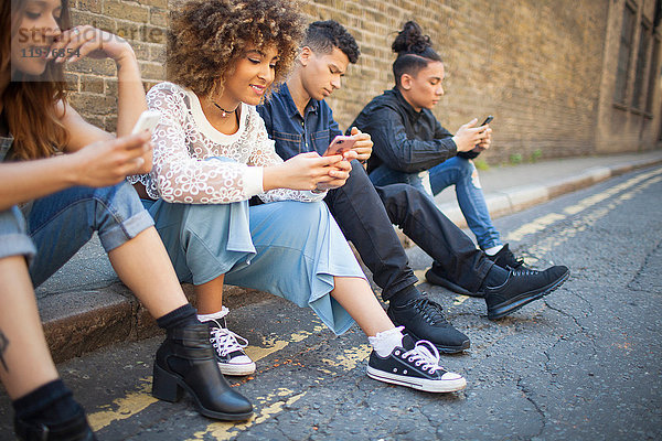 Vier Freunde sitzen auf der Straße und schauen auf Smartphones