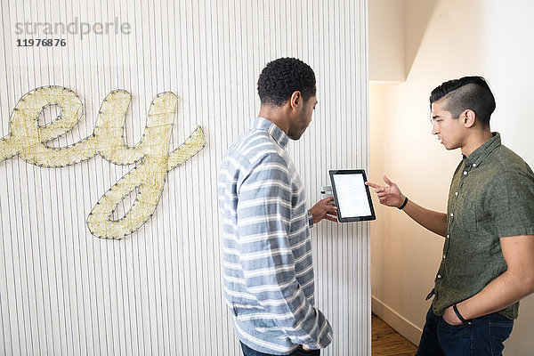 Coole junge Geschäftsleute im kreativen Büro schauen sich digitales Tablet an