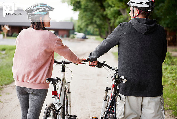 Älteres Paar zu Fuß mit Fahrrädern  Rückansicht