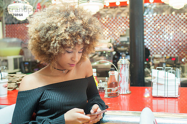 Junge Frau sitzt im Diner und schaut auf ein Smartphone
