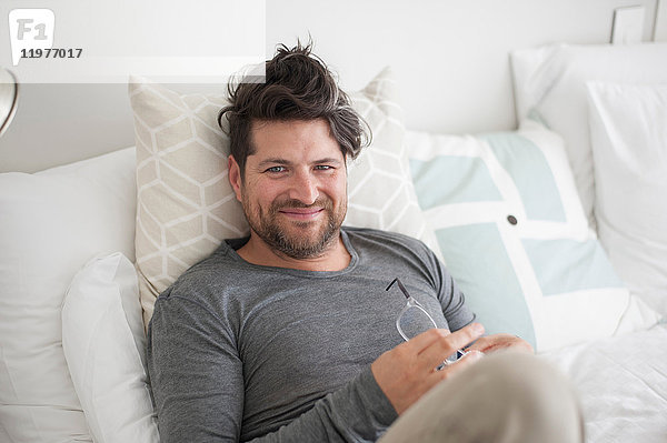 Porträt eines Mannes im mittleren Erwachsenenalter  der auf dem Bett liegt und sich auf dem Bett entspannt