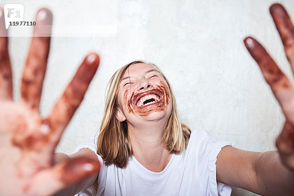 Porträt einer Frau mit Schokolade an den Händen und um den Mund  die Hände in Richtung Kamera haltend  lachend