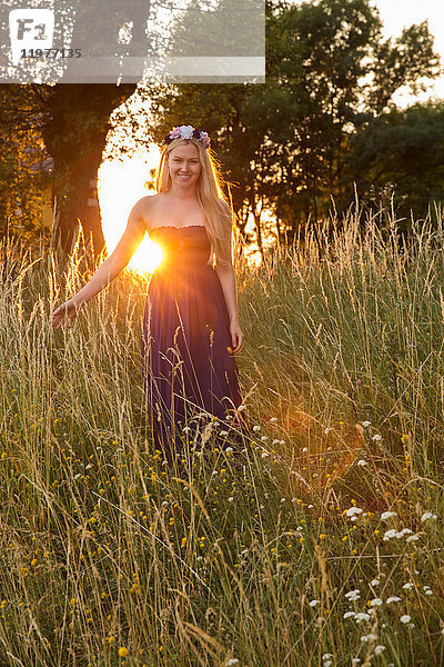 Frau trägt trägerloses Kleid im hohen Gras und schaut lächelnd in die Kamera