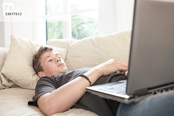 Teenager liegt auf Sofa und schaut auf Laptop