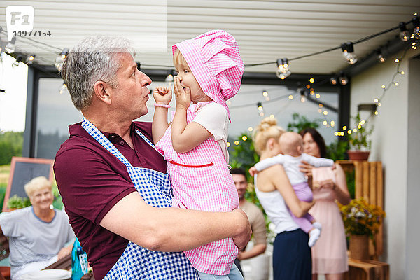 Erwachsener Mann schneidet Grimassen bei Kleinkind-Enkelin beim Familienessen auf der Terrasse